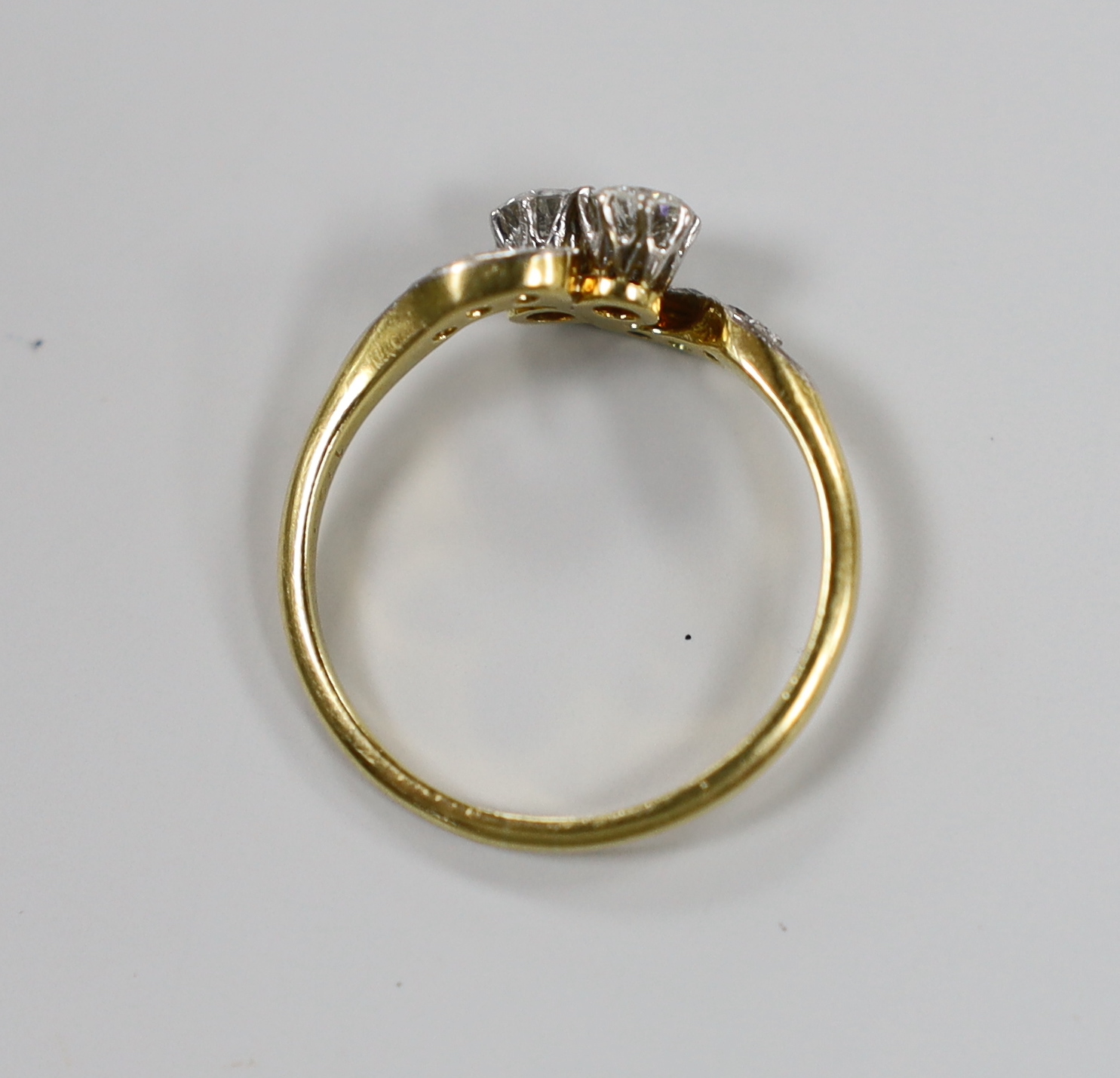 An 18ct, pt and two stone diamond set crossover ring, with diamond chip set shoulders, size P, gross weight 2.8 grams.